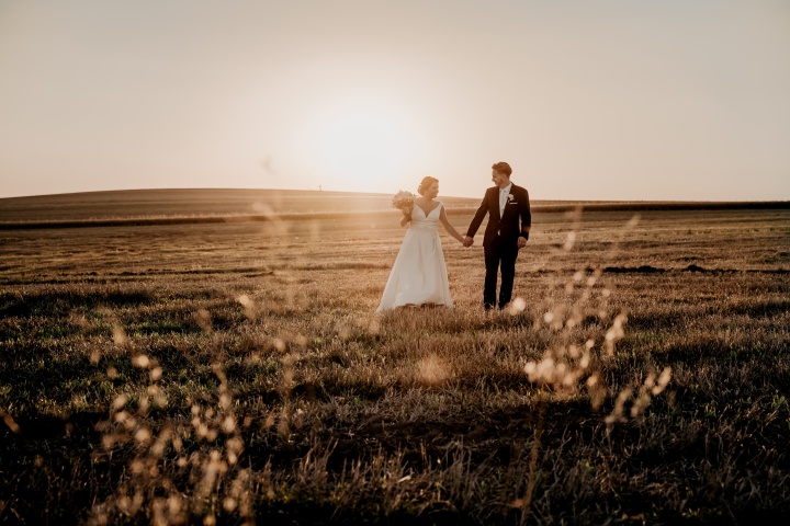 a bride and groom walking in an empty field at sunset