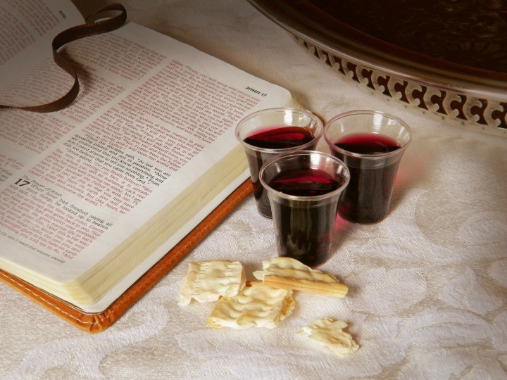 An open Bible with small cup of wine and unleavened bread.