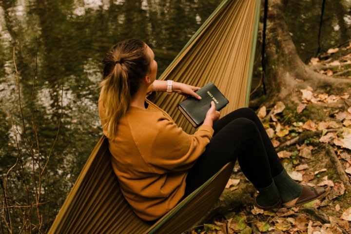 A woman sitting in a hammock holding a Bible.