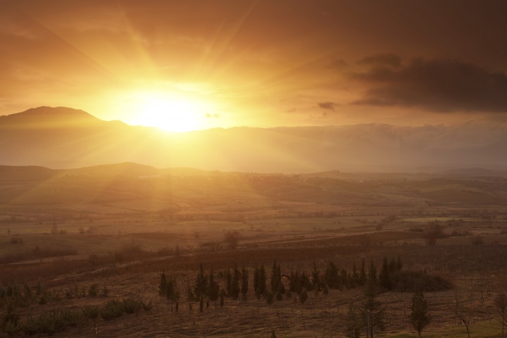 A sunrise coming over a mountain top lighting up the valley below.