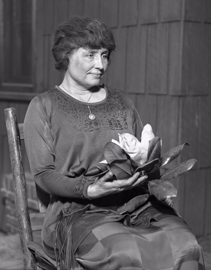 Helen Keller sitting, holding a magnolia flower, circa 1920.