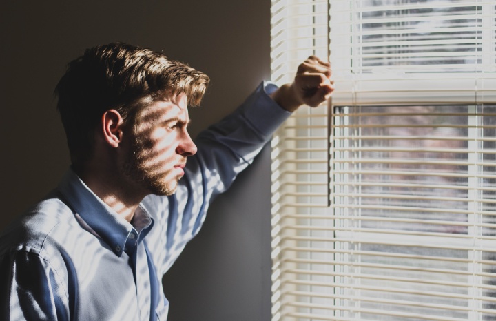 a man lifting a slat on the set of blinds on a window to look outside