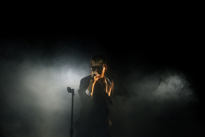 A man singing into a microphone on dark foggy stage.