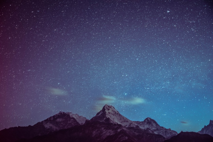 Stars in a night sky with mountain peaks in the foreground. 