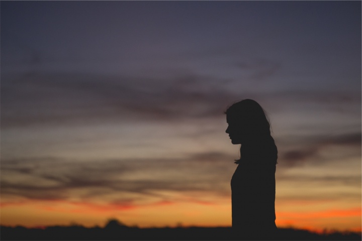 The silhouette of a young woman with the sun setting in the background.