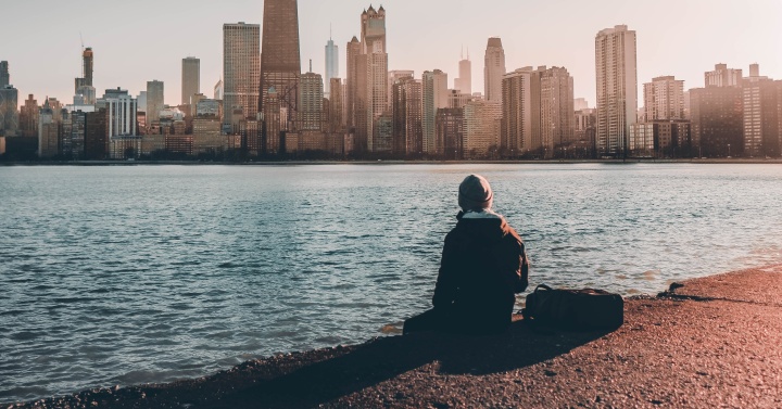 A person sitting near the edge of water looking at a city skyline.