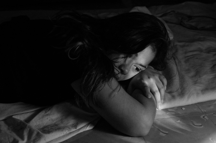 A woman laying on a bed looking depressed.
