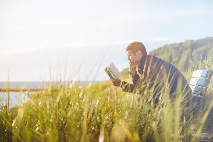 A man reading a Bible sitting on a park bench.