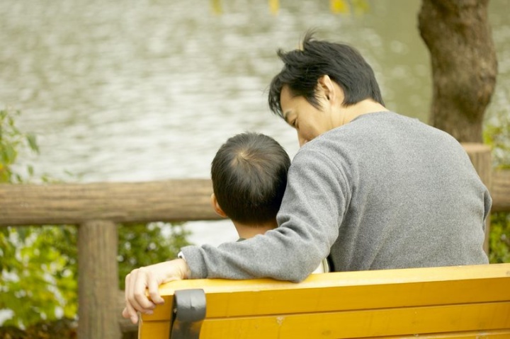 A father and son sitting together on a park bench.