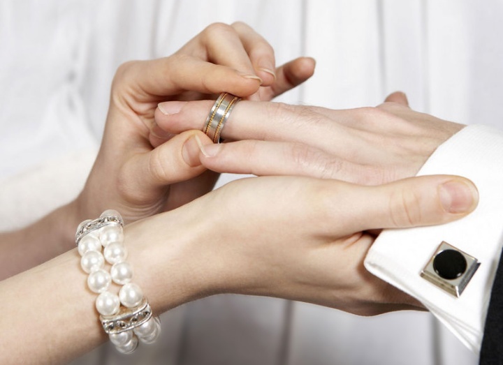 A woman putting a wedding ring on her husband.