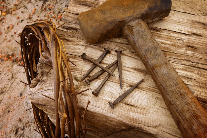 Photo illustration of a crown of thorns, old nails, hammer and wood beam.