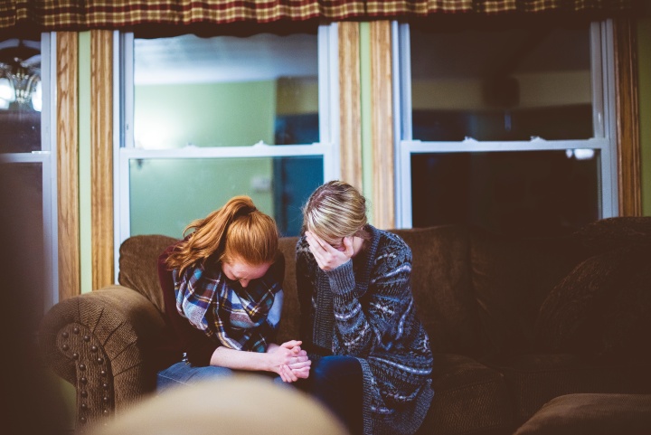 Two women sitting together on a couch crying.