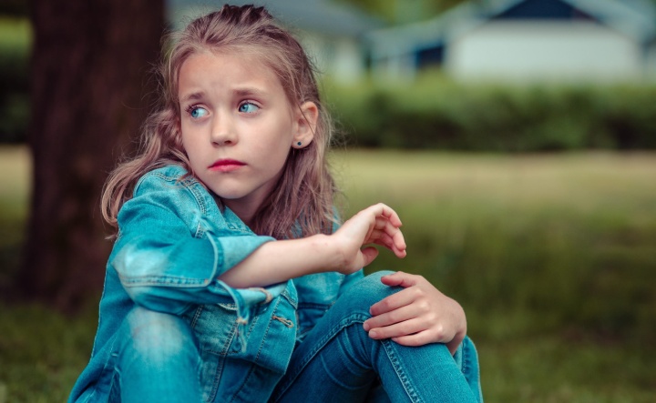 A little girl sitting on the grass looking sad.