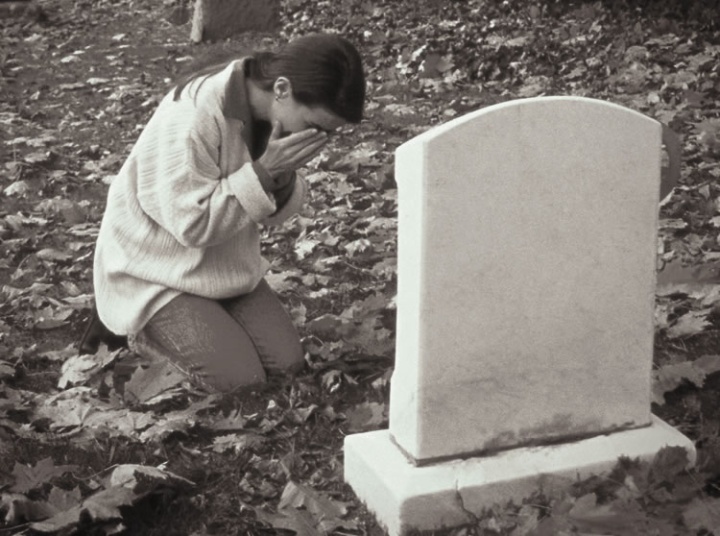 A woman crying by a grave stone.