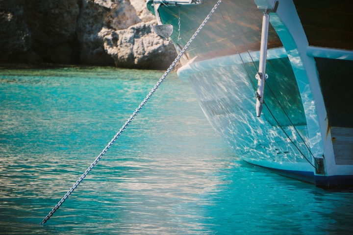 A boat in the water with a chain going down into the water attached to an anchor.