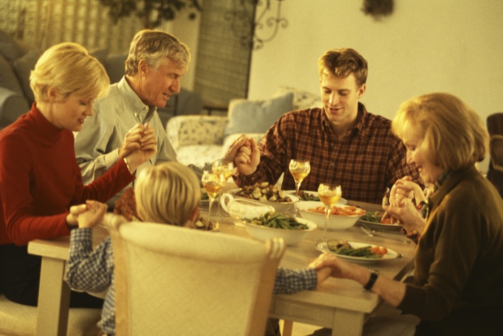 A family holding and praying before eating a meal.