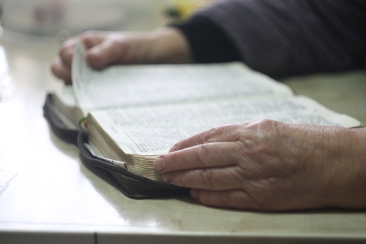 An old person's hands hold the edges of a Bible.