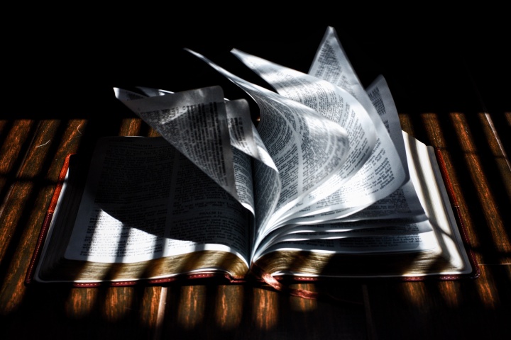 A Bible laying on table and the pages are blowing in a breeze.