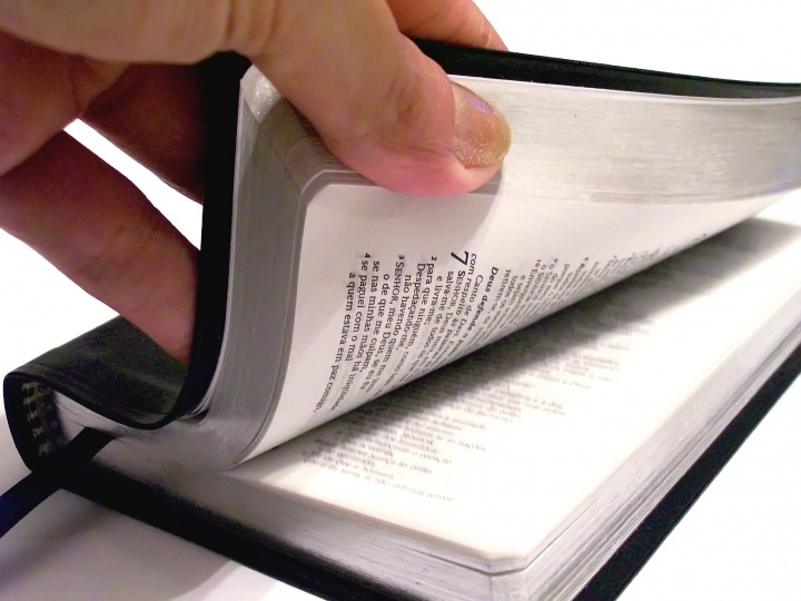 A person's hand thumbing through a Bible. 