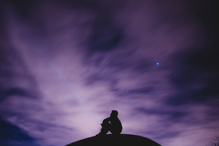 A person sitting on a hill with the stars in background.