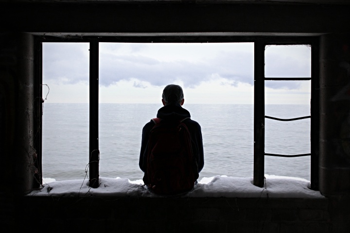 A teen sitting in abandoned window frame of an old house.