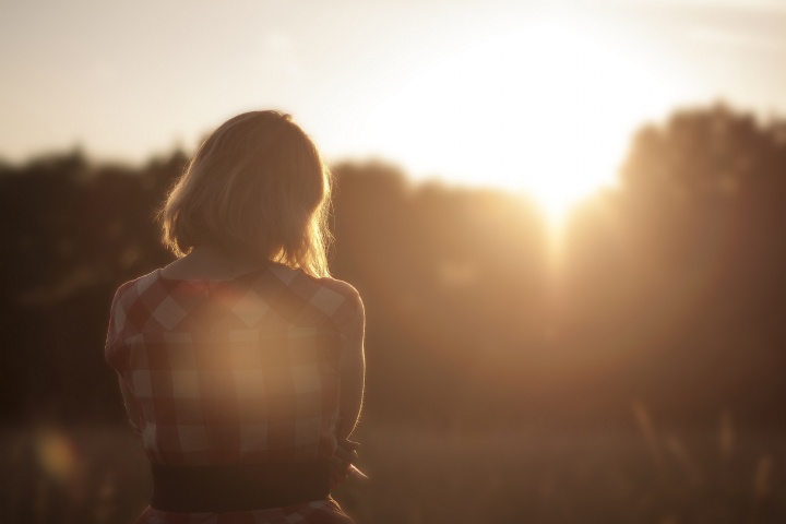 A woman looking at trees with sunrays shining through.