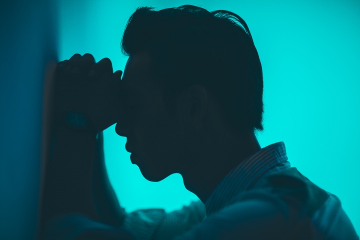 A man with his head and hand resting against a wall.