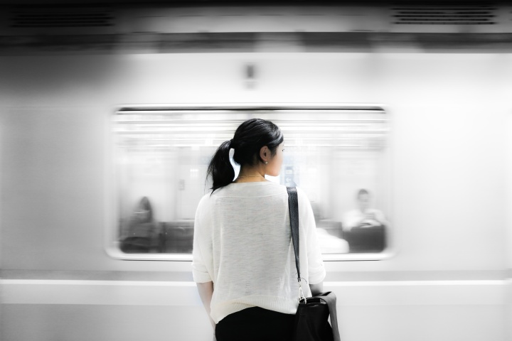 A woman standing has a train speeds by.