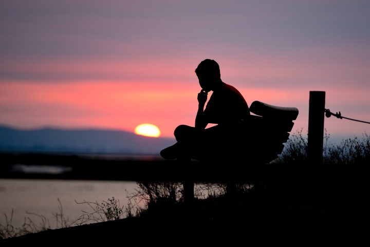 A person sitting on a bench with the sun setting.