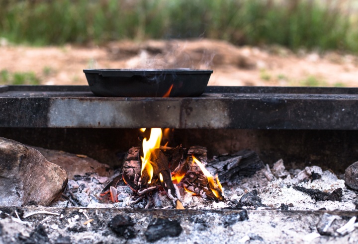 A cast iron skillet on a fire grate with hot flames underneath.