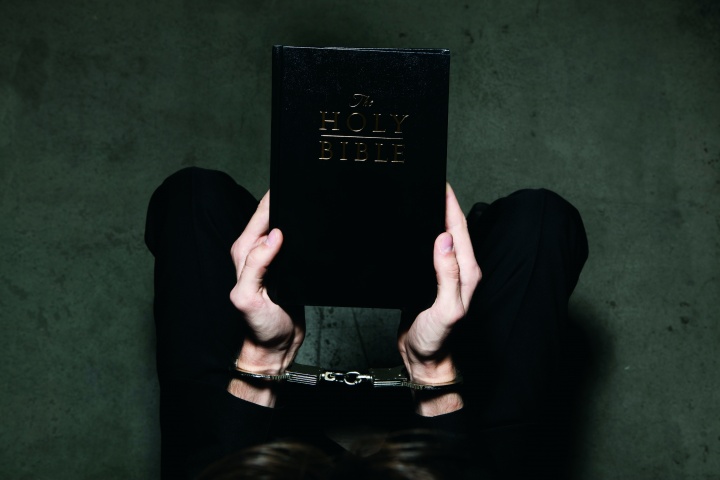 A person holding a Bible while their hands are wearing shackles.