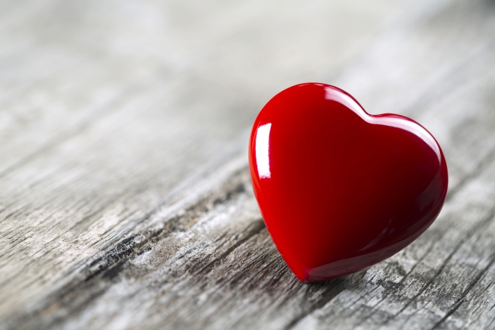 A round red heart laying on wood table.