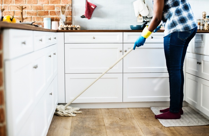 A person cleaning a kitchen floor with a mop.