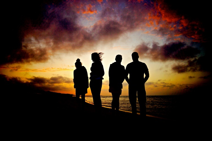 A silhouette of four people at dusk near a body of water.