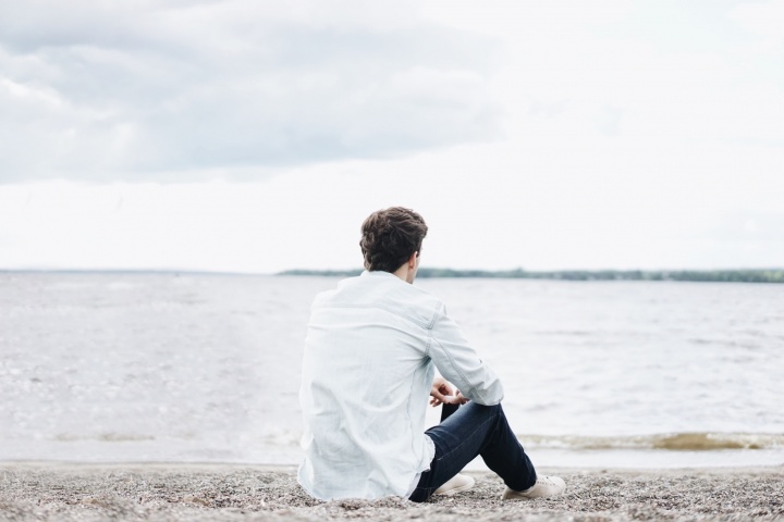 A young man sitting on the shore a lake - looking at the water.