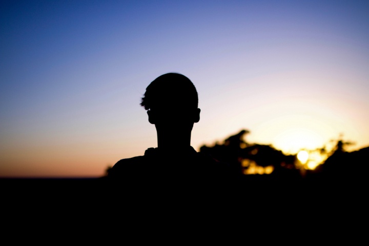 A shadow of young man looking towards the sunset.