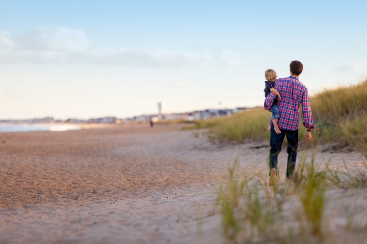 A father carrying his small child on the beach.