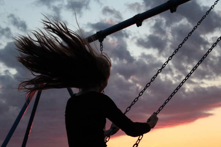 A woman swinging on a playground swing at sunset.