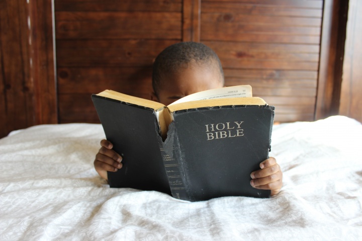 A little lying in bed looking at a Bible.