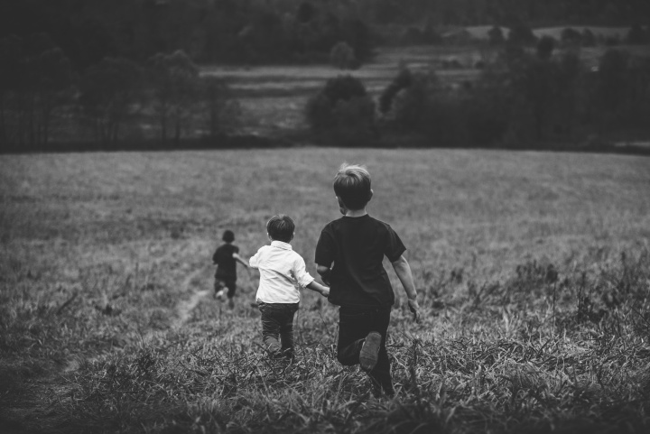 Three young boys running through a field of tall grass.