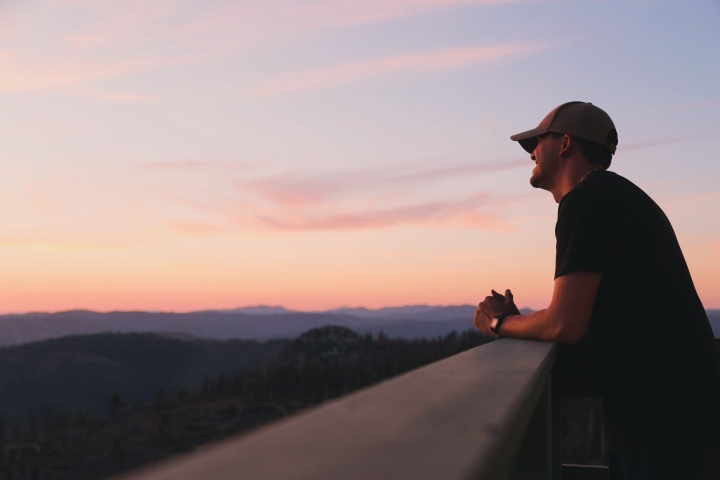 A young man watching the sun set from an observation deck.