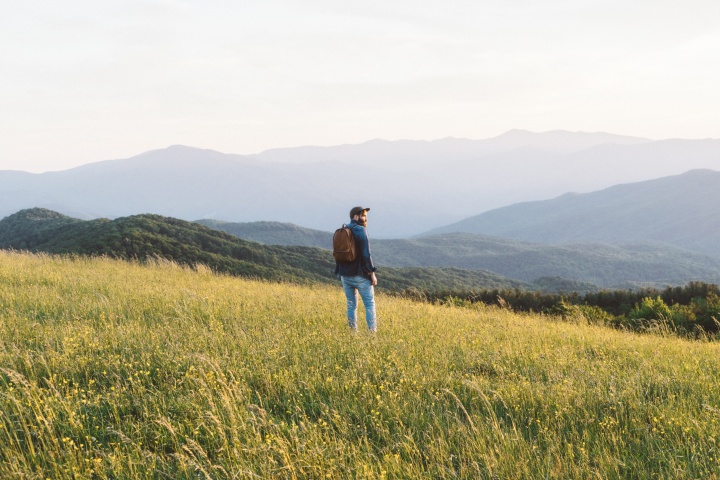 A man hiking in field with mountains in the background.