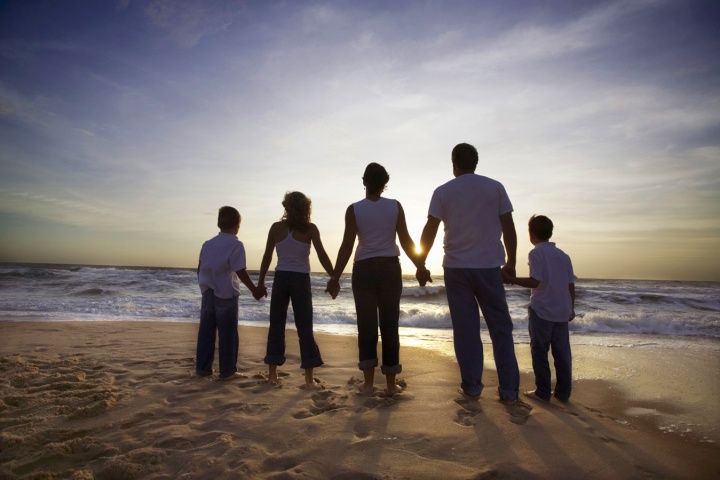 A family holding hands looking at the ocean waves and the sun setting.