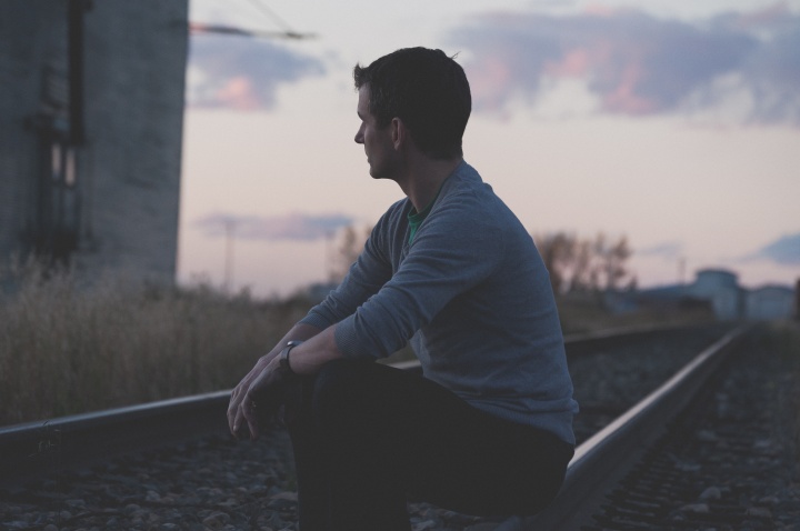 A young man sitting by an old railroad track.