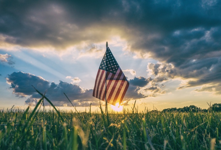 A small United States flag in the grass with the sun setting in the horizon.
