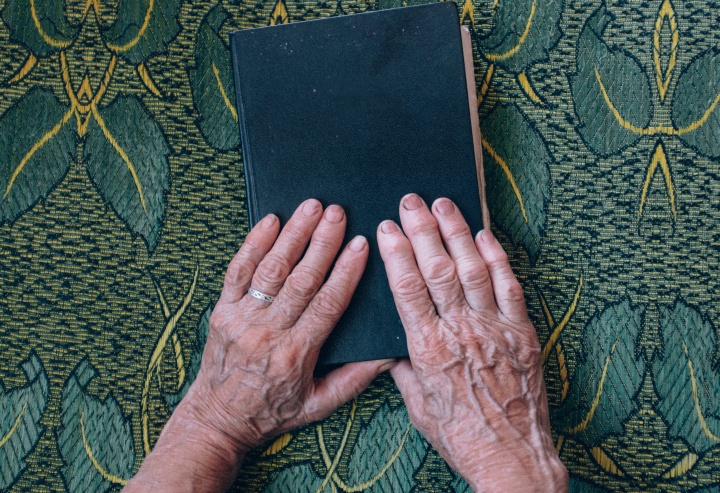 An older woman's hands resting on top of a Bible.