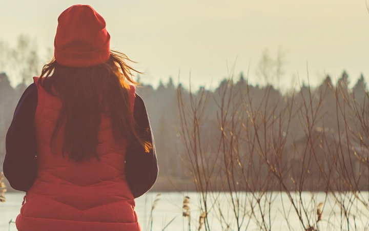 A woman wearing a jacket sitting outside looking at a lake.