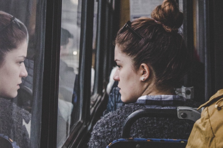 A young woman riding a bus and looking out the window.