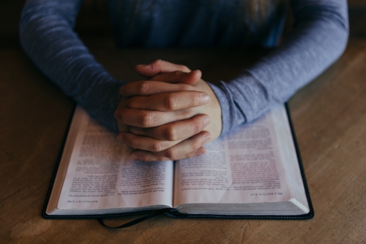 A woman praying with her hands on a Bible.