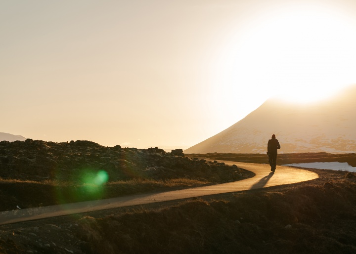 A person walking on a narrow road with the sun setting in the background.